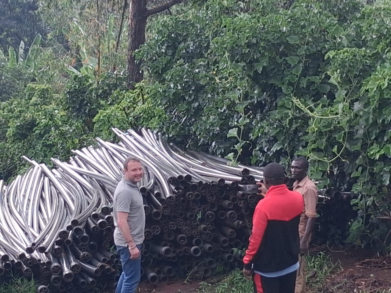Canalisations livrées au Burundi, stockées en bord de végétation, avec trois personnes